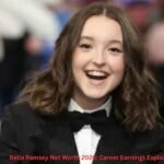 Bella Ramsey smiling at a red carpet event in a black tuxedo while attending a public appearance, featured in an article about Bella Ramsey Net Worth and career earnings.